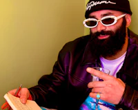 Alternative pop artist Nevv Evve developing songwriting concepts and creative direction during a collaborative live session while wearing a Supreme hat along with luxury accessories and holding his notebook and a glass.