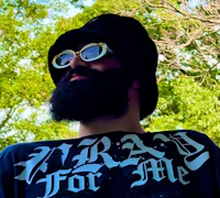 Nevv Evve wearing a black bucket hat and white sunglasses outdoors, looking upward beneath green trees, representing upcoming music releases and future projects.