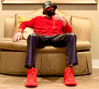Nevv Evve seated in a red Balenciaga sweater and red Balenciaga shoes while promoting upcoming live events, performances, exclusive experiences, and VIP subscriber opportunities.